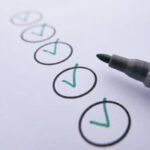 Close-up of a checklist with green checkmarks on white paper using a marker.