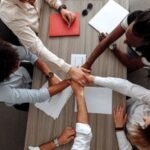 Overhead view of a diverse team placing hands together in a sign of unity during a meeting.